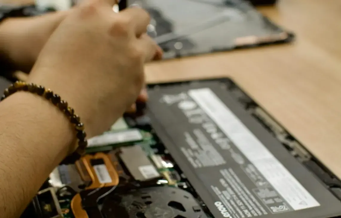Technik serwisu wymienia podzespoły w otwartym laptopie Lenovo — widoczna bateria i płyta główna