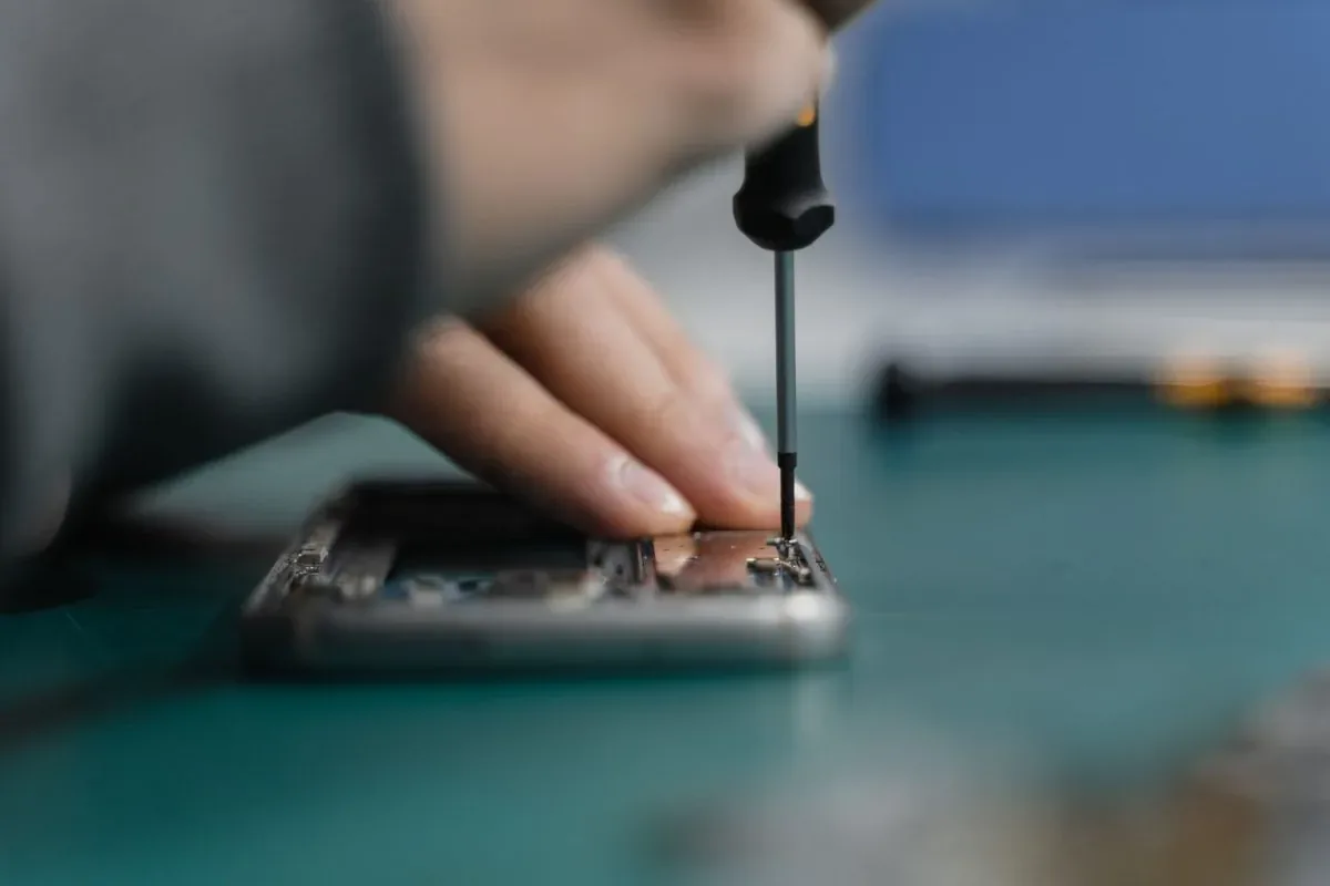 Dłonie naprawiające rozebrany telefon śrubokrętem precyzyjnym
