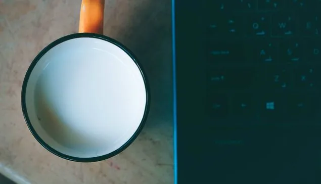 Kubek z mlekiem stojący tuż obok otwartego laptopa z klawiaturą — laptop działał tydzień po zalaniu i nagle przestał — dlaczego
