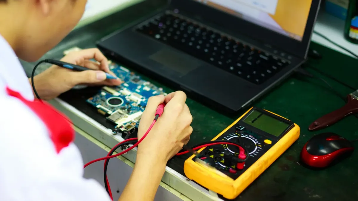 Technik testujący płytę główną laptopa multimetrem obok otwartego notebooka — druga próba po nieudanej naprawie w innym serwisie