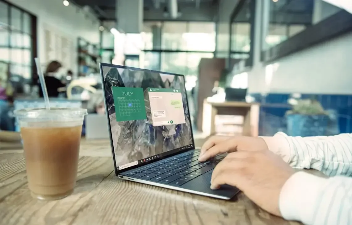 Dłonie piszące na laptopie z kawą w kawiarni, ekran z kalendarzem — ekran działa poprawnie tylko pod pewnym kątem