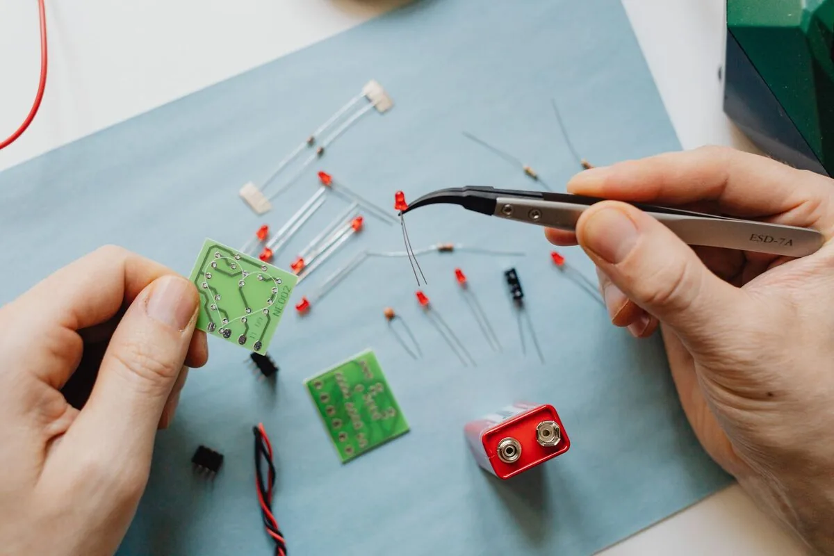 dłonie trzymające pęsetę i miniaturowe płytki elektroniczne z baterią — naprawa układu ładowania baterii na płycie głównej